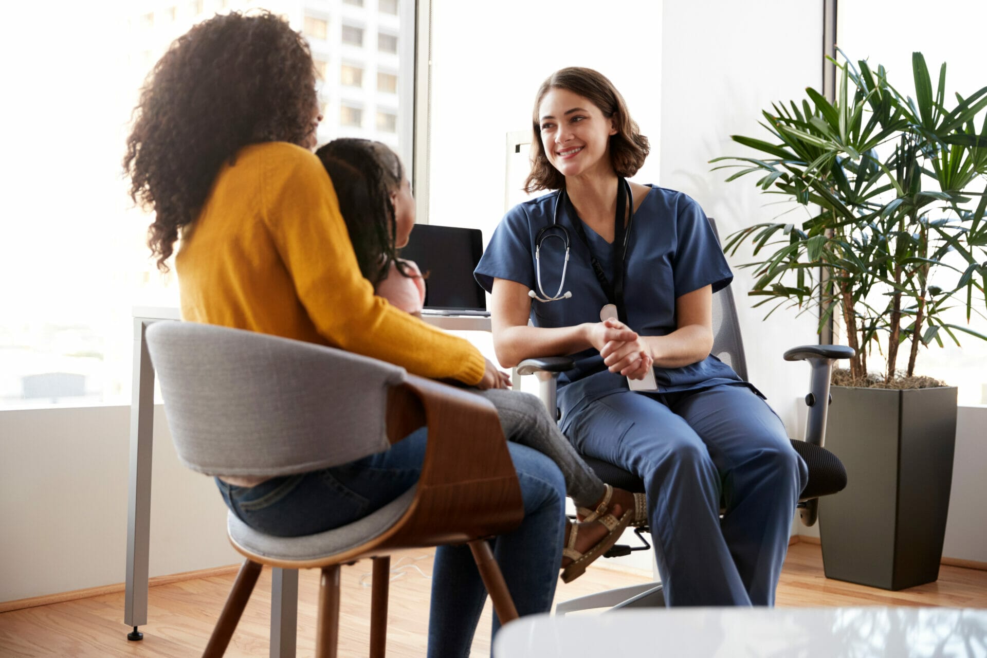 Mother And Daughter Having Consultation With Female Pediatrician Wearing Scrubs In Hospital Office