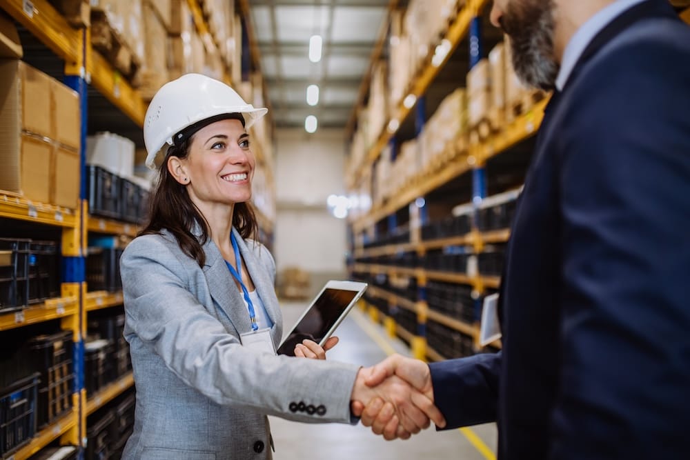 Managers in suits shaking hands in a warehouse.