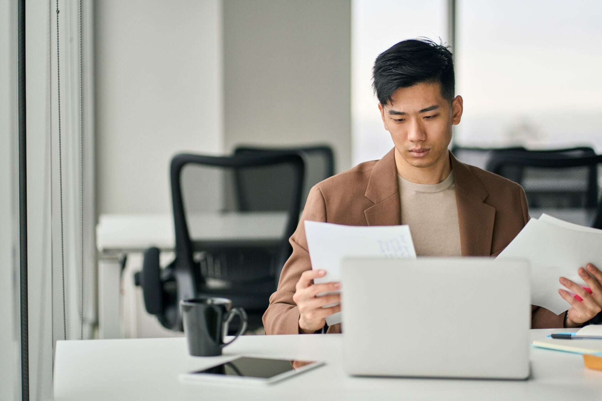 Man in light brown suit jacket and beige shirt looking at paperwork, focused