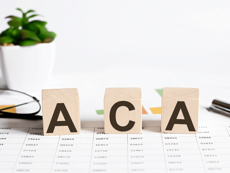 ACA spelled out with blocks sitting on desk with glasses and a plant