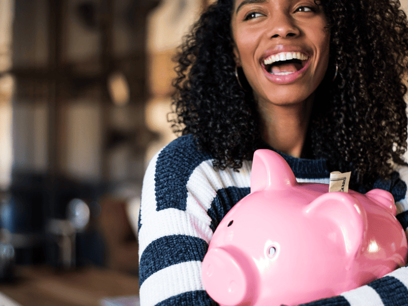 Woman holding a pink piggy bank smiling laughing