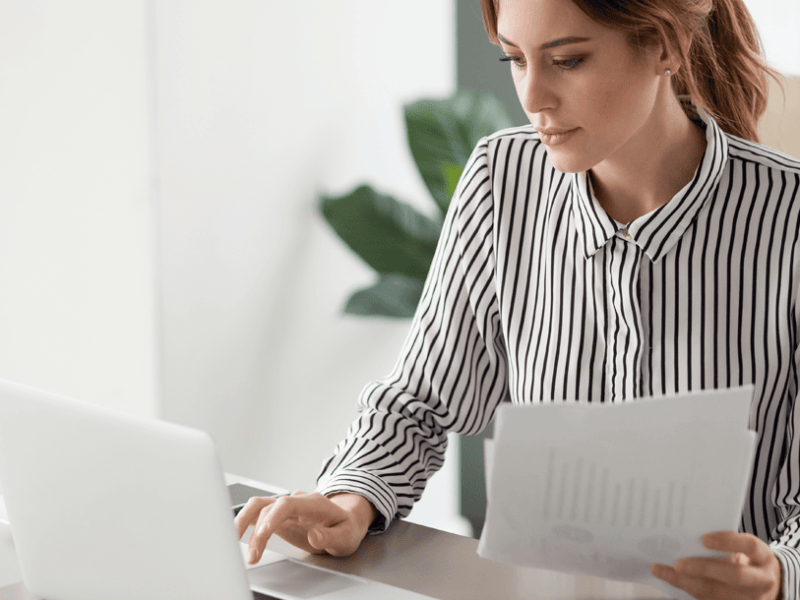 woman typing on laptop holding papers