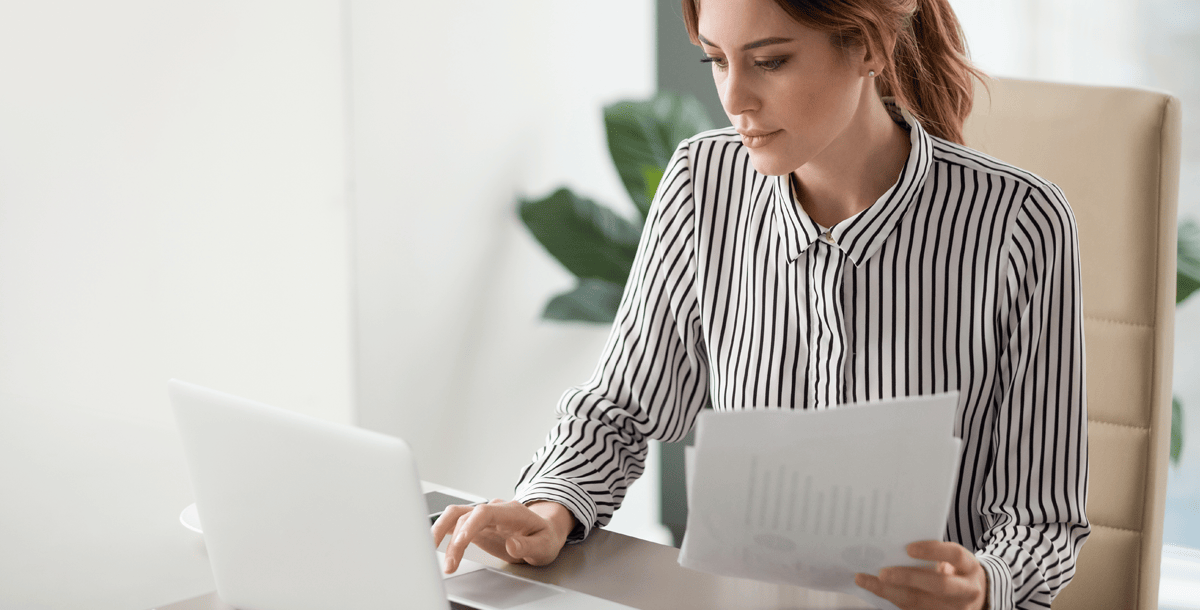 woman typing on laptop holding papers