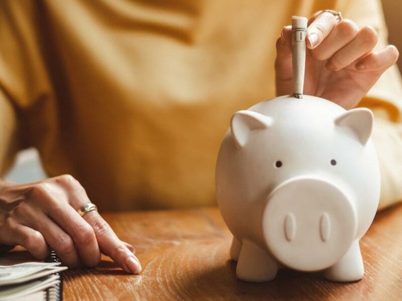 woman inserting money into a white piggy bank