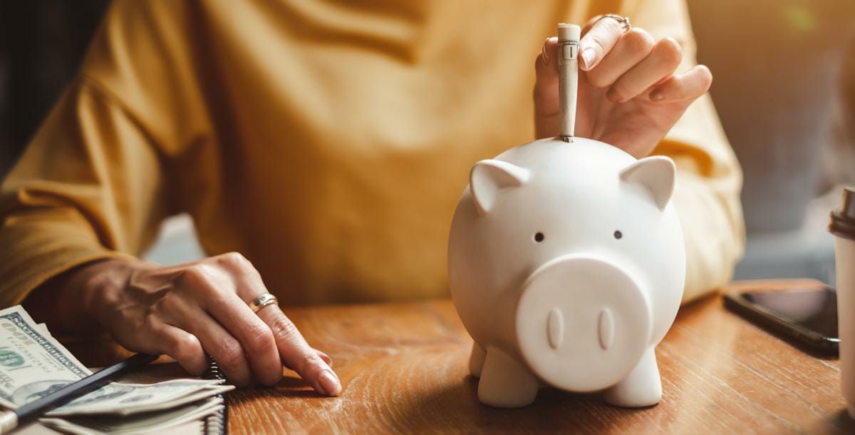 woman inserting money into a white piggy bank